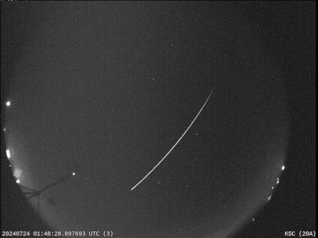 A bright meteor streaks across the dark night sky, leaving a trail of white light.