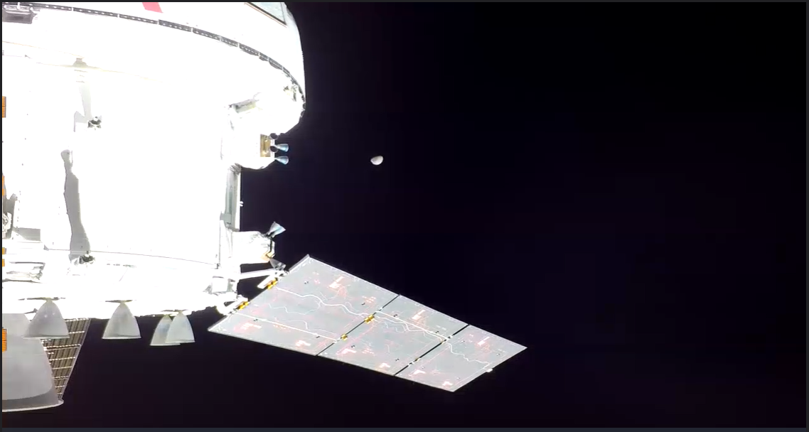 Orión, en el primer plano de la imagen, es de un blanco brillante en contraste con la oscuridad del espacio.  La Luna está aproximadamente 3/4 iluminada a la derecha de la nave espacial, aún a más de 100 000 millas de distancia.