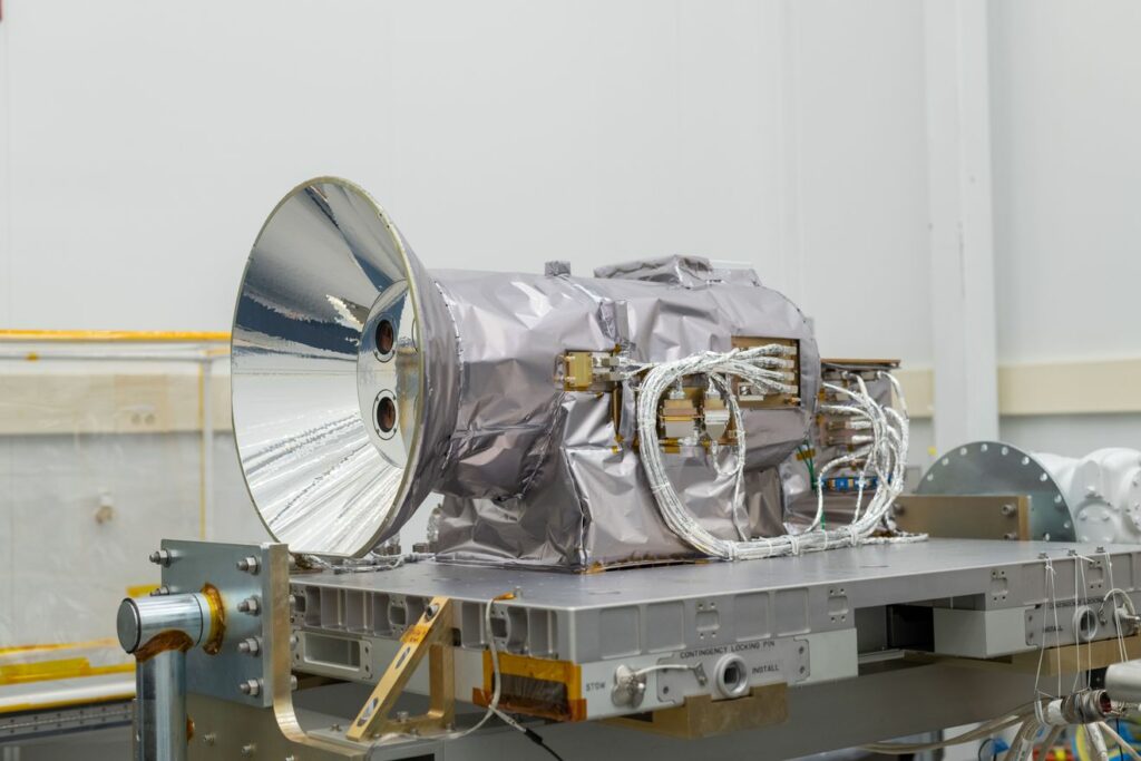 The AWE instrument appears wrapped in silver metallic blankets as it lays horizontally on a metal platform in a large clean room.