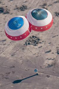 A pair of parachutes lower the dart-shaped test vehicle to the ground to conclude the drop test for a modified parachute for the Starliner spacecraft.