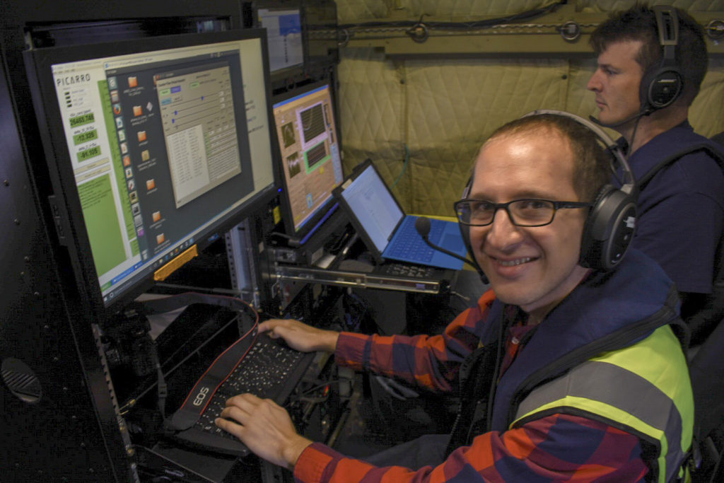 Image 3: Michael Diamond (front) operating a Counterflow Virtual Impactor Inlet System (CVI), which lets instruments make aerosol measurements within the clouds, and Steve Broccardo (back) operating the 4STAR (Spectrometers for Sky-Scanning, Sun-Tracking Atmospheric Research) instrument, a sunphotometer that can measure smoke properties at multiple wavelengths of light, aboard the P-3 on the October 10th, 2018, ORACLES flight. Photo credit: Andrew Dzambo