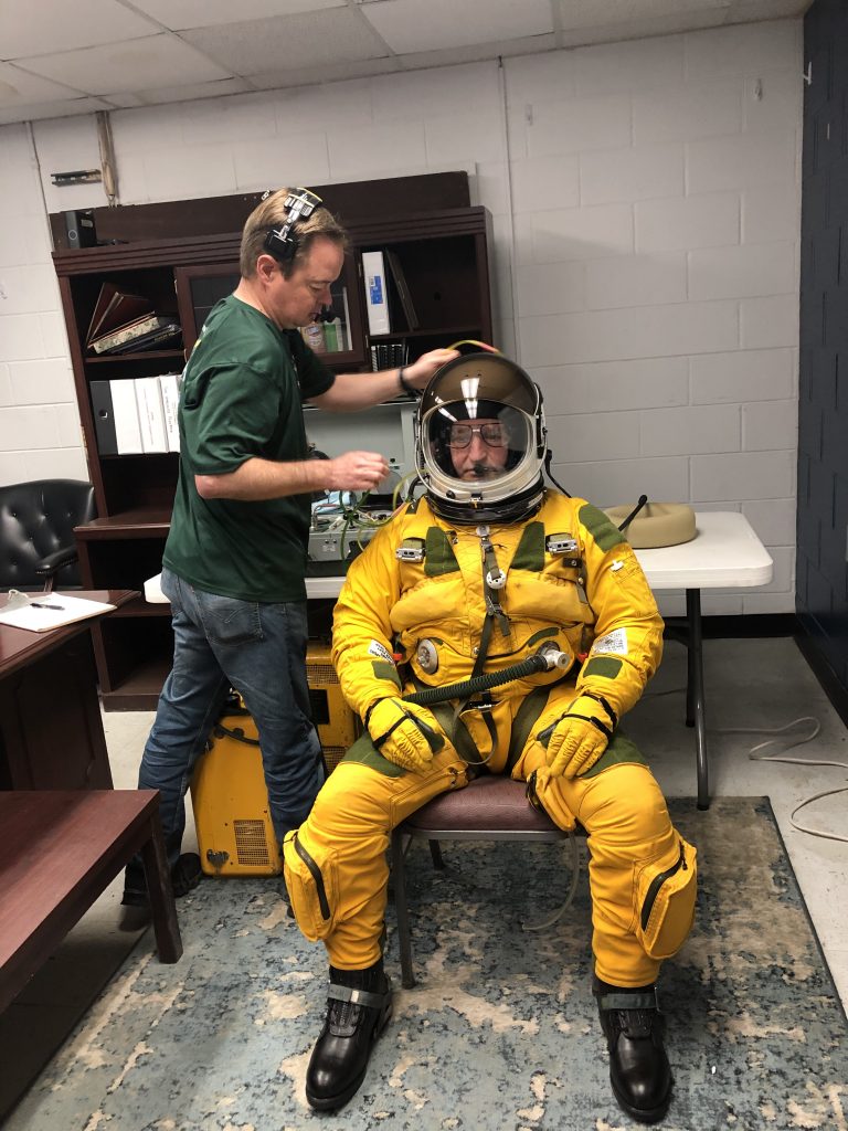 Joey Barr making sure that Cory Bartholomew is happy with his glasses. Once the helmet is shut, the pilot will not open the visor again until after landing. Credit: NASA/Katie Stern