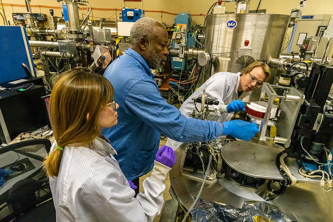 Three scientists installed the white and red HIT instrument (right side of image) into a vacuum chamber (silver machinery on right-side of image).