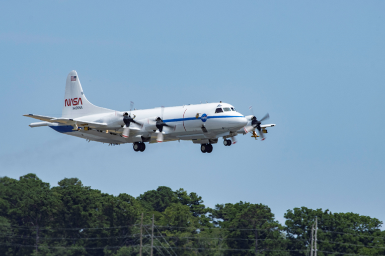 A large white aircraft with NASA logos upon it flies through the air. 