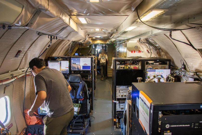 The interior of a scientific aircraft. Multiple screens and exposed cables are visible throughout. 