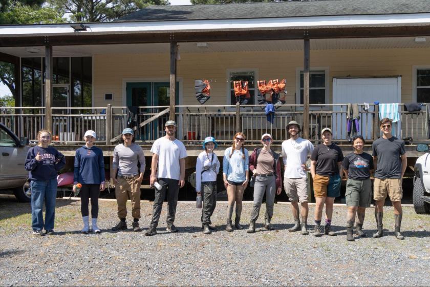 A group of muddy students pose together in a parking lot and smiles. 