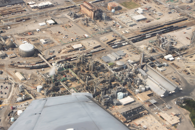 A large industrial zone is viewed from the sky. Large domes and pipes are seen throughout. 