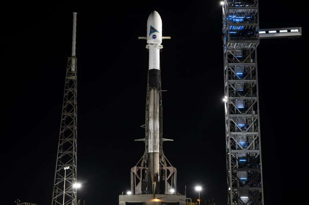 A Falcon 9 rocket stands on a launch pad with a black back ground from the darkness.