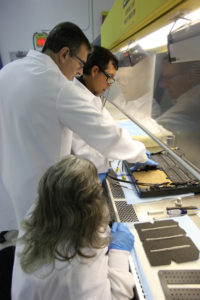 Dr. Oscar Monje, (far left) a research scientist, packs a growing substrate called arcillite in the science carrier, or base, of the Advanced Plant Habitat (APH) inside a laboratory at the Space Station Processing Facility at Kennedy Space Center. Assisting him is Jeffrey Richards, project science coordinator with SGT on the Engineering Services Contract. Seated in the foreground is Susan Manning-Roach, a quality assurance specialist, also with ESC.