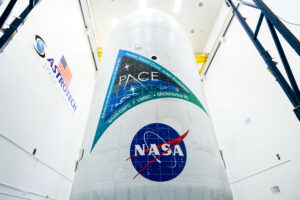 A SpaceX Falcon 9 payload fairing with artwork of NASA's PACE mission.