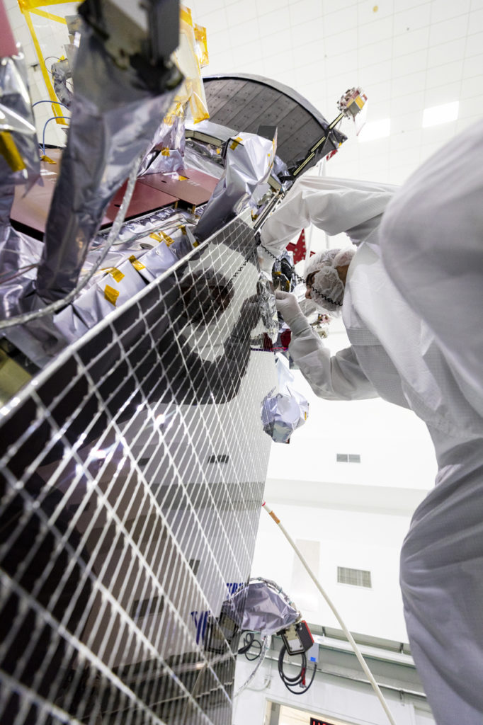 A view from the bottom of a solar panel, looking up as a person in a bunny suit works on the top of the panel.