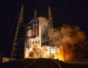 The Delta IV Heavy carrying Parker Solar Probe lifts off the pad as smoke billows beneath it. 