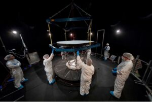 People wearing protective white clothing stand around pieces of Parker Solar Probe in a dark room.