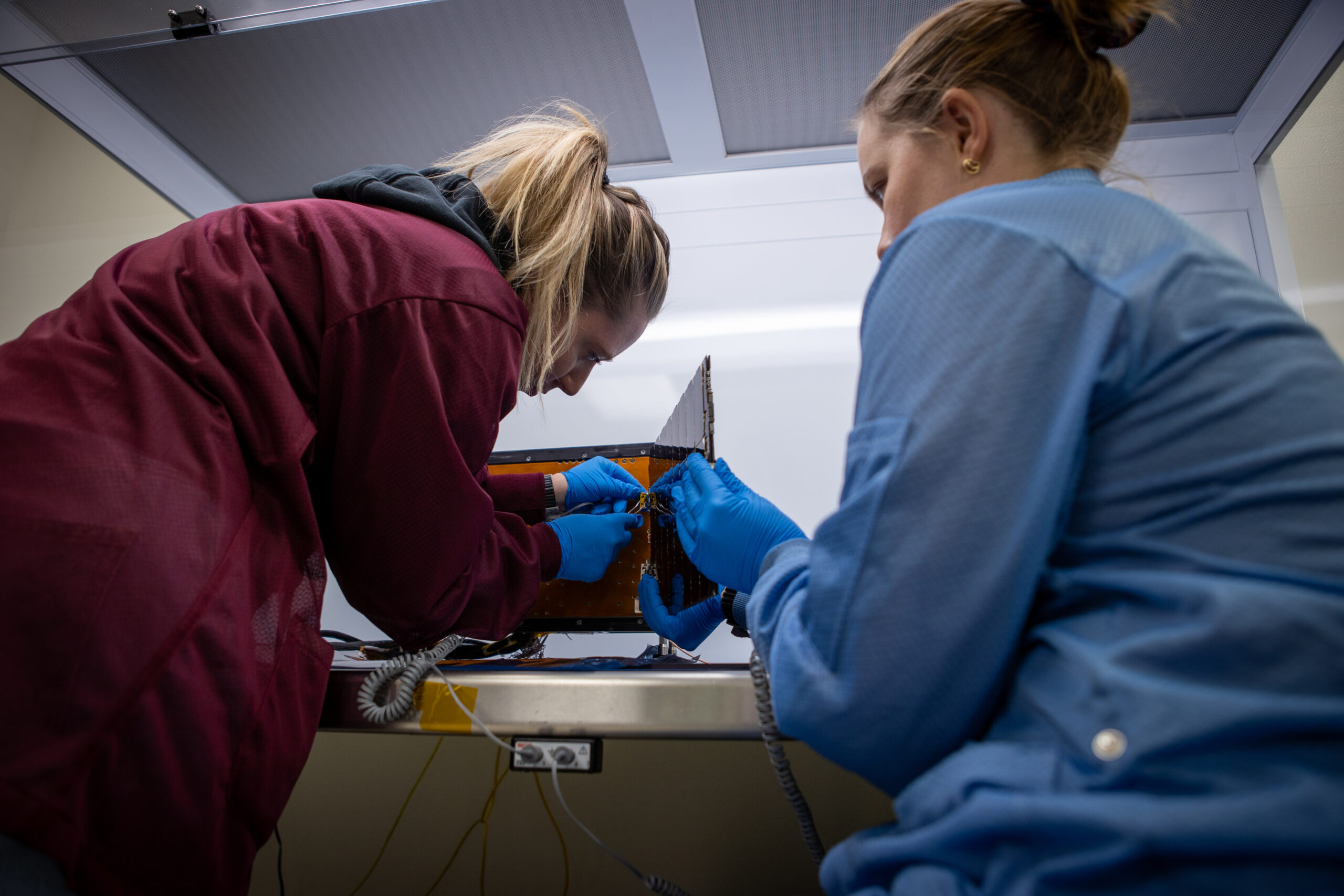 This photograph shows two women working on a small spacecraft.