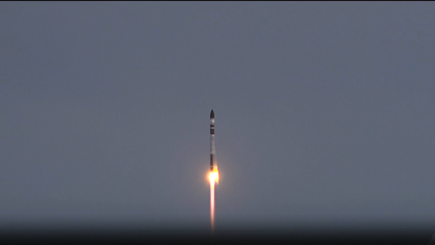 A Rocket Lab Electron rocket lifts off from the pad amid an overcast sky.