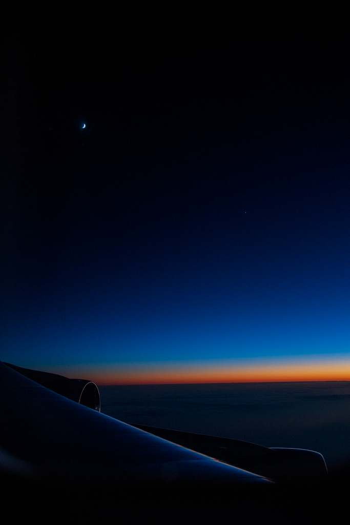 Image through one of SOFIA’s windows, overlooking over one wing with two of the engines in view. The colorful sunset sky and the crescent moon are visible as the team prepares to observe Venus.