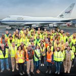 Deployment crew and staff stand in front of the SOFIA aircraft, all wearing neon yellow high-vis vests and jackets.