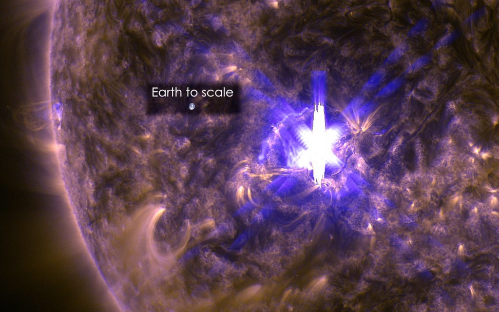 An image of the Sun, with a flare exploding. Earth is shown to scale, smaller than the flare.