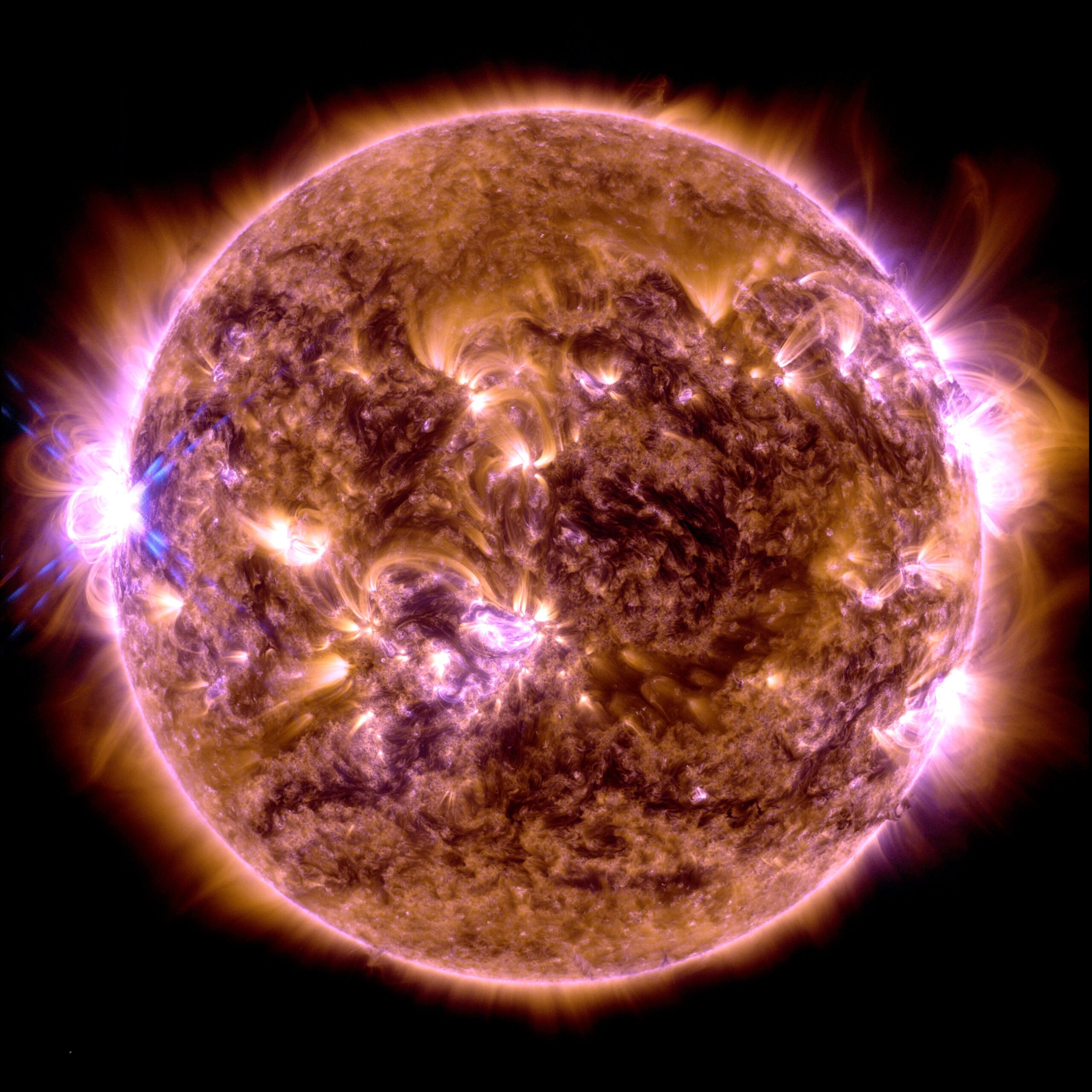 Close up image of the Sun colorized in a mix of yellow, orange, brown and black that showcases the dynamic beauty of the Sun. The X5.0 flare appears as a bright white flash on the left side of the image.