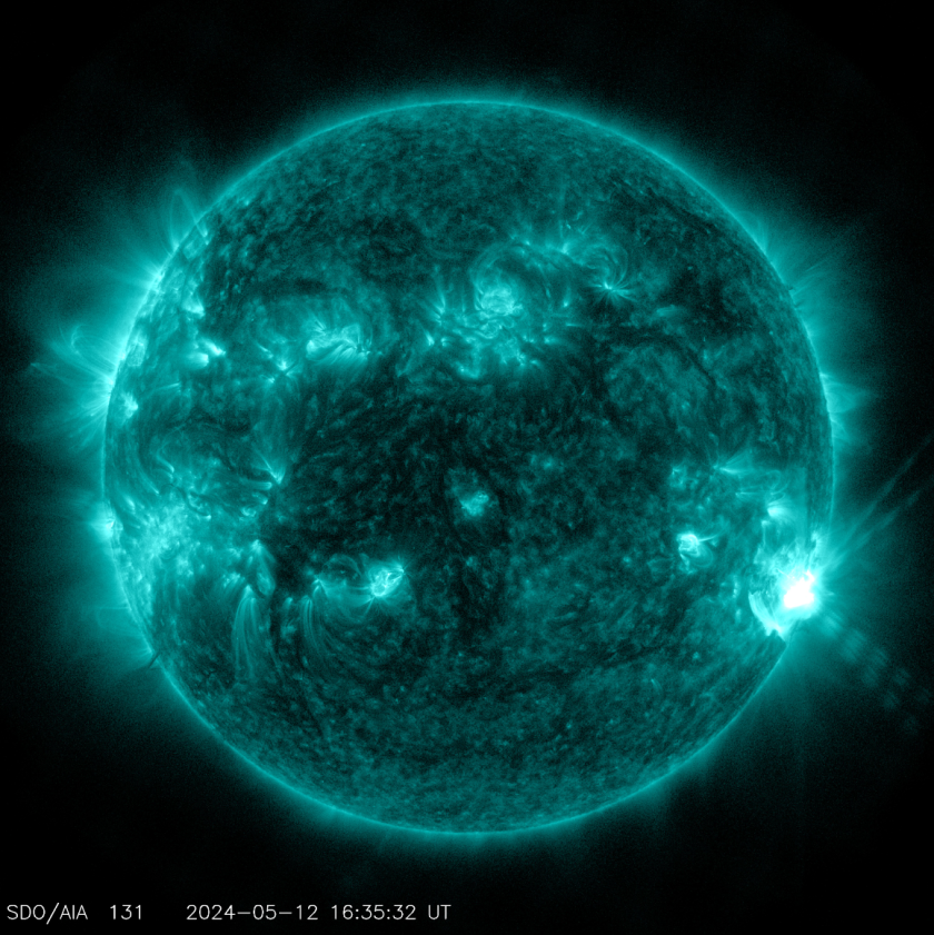 The disk of the Sun, colorized in teal, features a bright flash on the lower right. Less intense bright spots and loops of material dot much of the Sun's surface. 