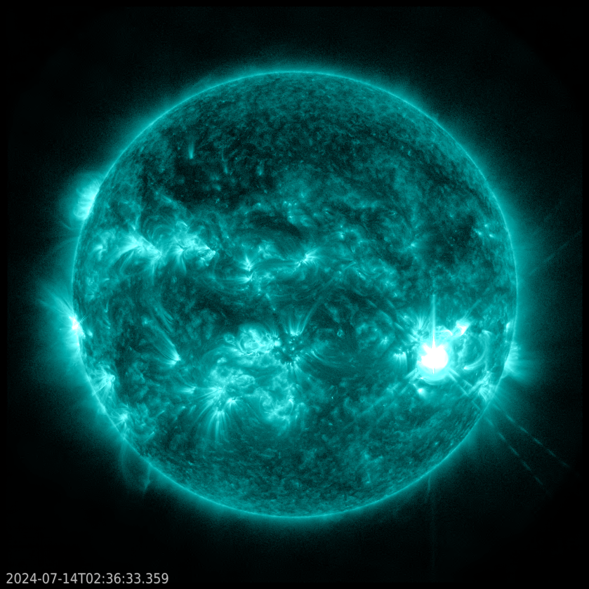 The Sun, shown in teal against a black back ground. The Sun is a mix of darker, almost black areas and bright teal regions. On the right is an extremely bright flash of white.