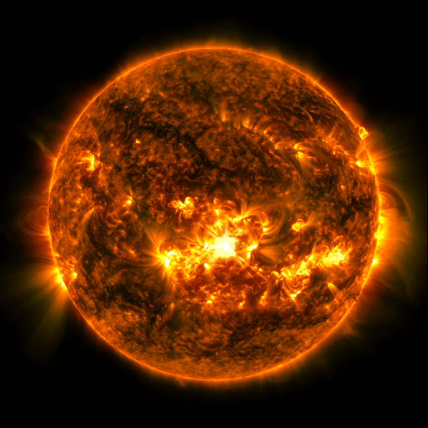 The Sun, shown in orange with dark splotches and bright yellow areas, against a black background. Toward the center of the star is a bright yellow area — the solar flare.