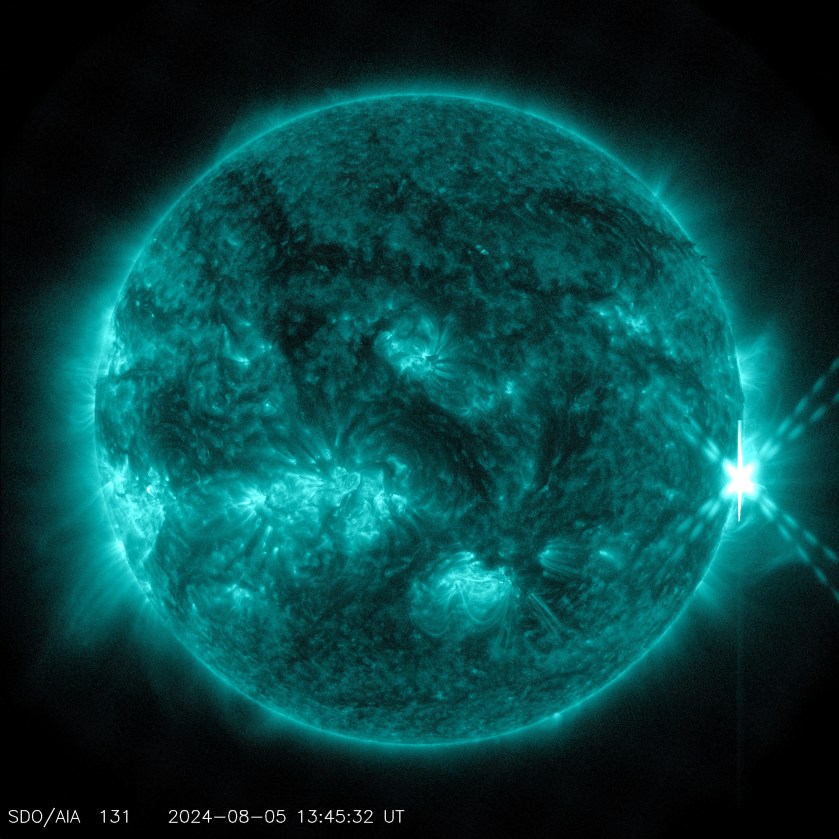 The Sun, shown in teal, against a black background. On the right side of the star, it a bright "X" shape — the solar flare.