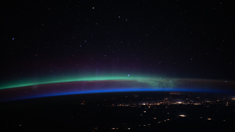 An aurora above the city lights and a beneath a starry sky