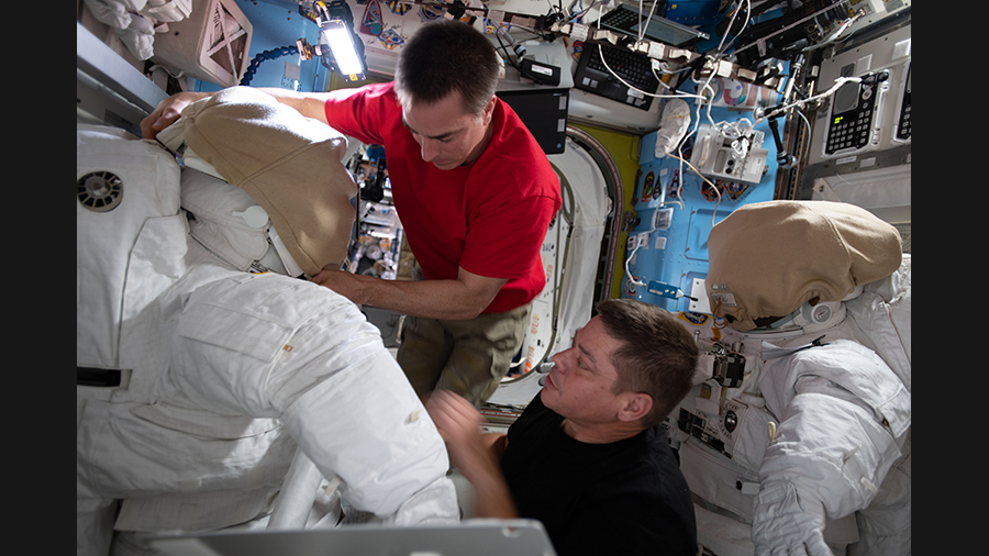 NASA astronauts (from top) Chris Cassidy and Bob Behnken work on U.S. spacesuits inside the International Space Station's Quest airlock.