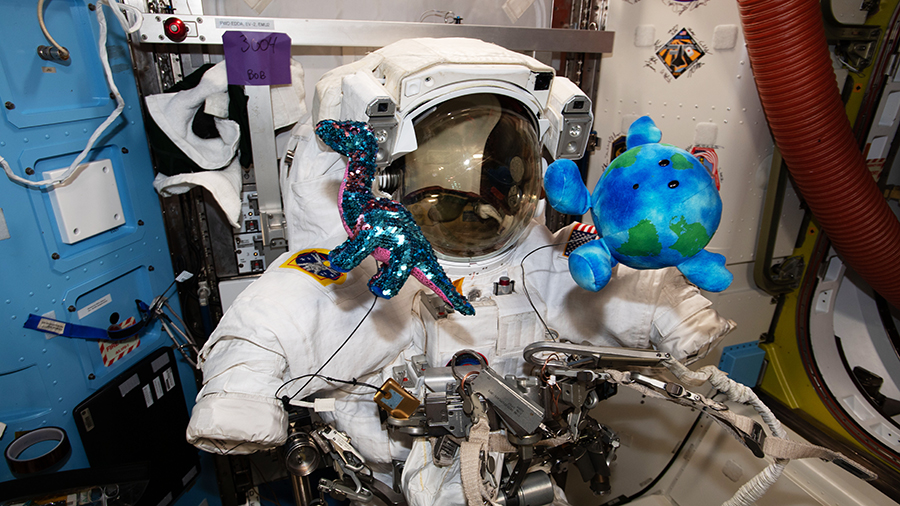 A U.S. spacesuit is pictured surrounded by a pair of plush-doll mascots