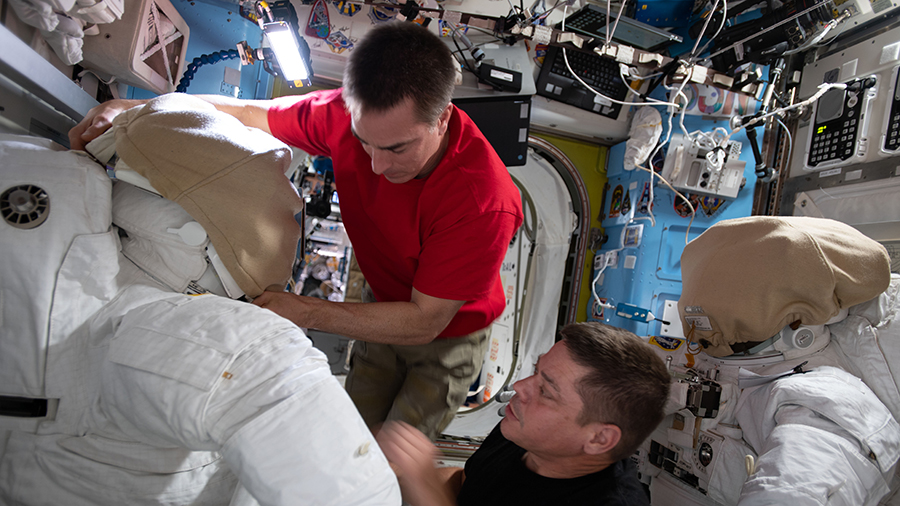 NASA astronauts (from top) Chris Cassidy and Bob Behnken work on U.S. spacesuits inside the International Space Station's Quest airlock.