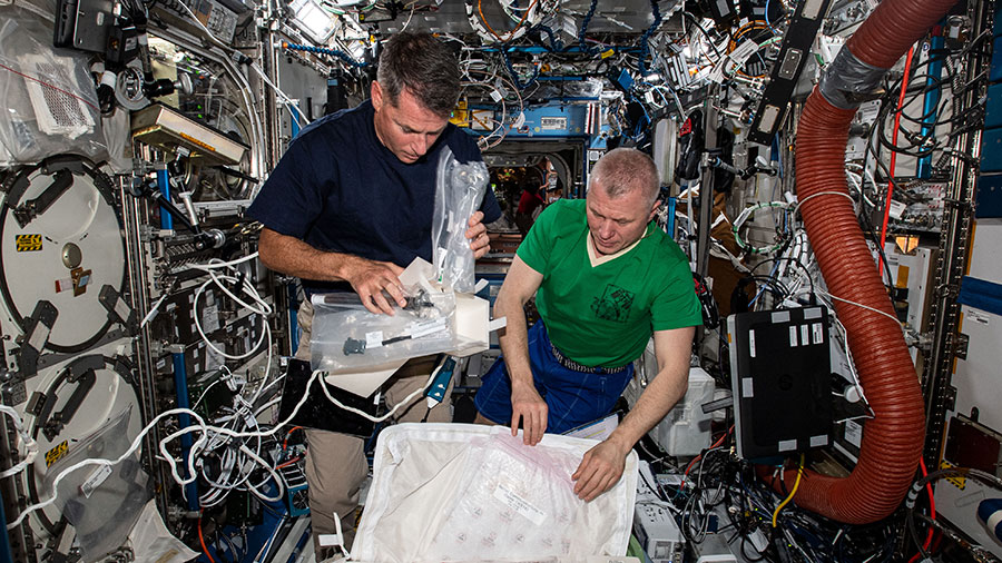 Expedition 65 Flight Engineers (from left) Shane Kimbrough and Oleg Novitskiy unpack science hardware for installation inside the U.S. Destiny laboratory module.