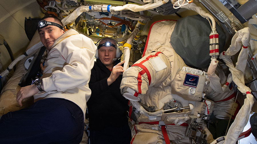 Cosmonauts (from left) Pyotr Dubrov and Oleg Novitskiy prepare Russian Orlan spacesuits inside the Poisk mini-research module for an upcoming spacewalk.