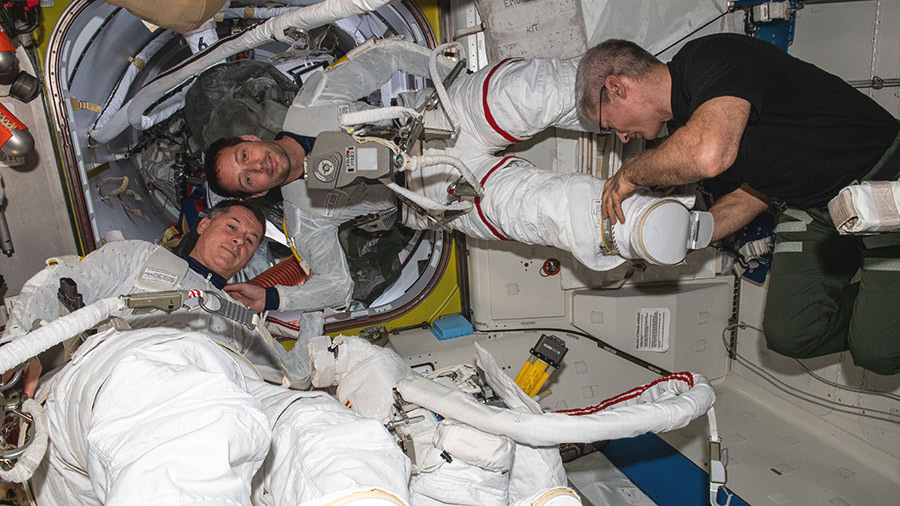 Expedition 65 Flight Engineer Mark Vande Hei assists astronauts Shane Kimbrough (bottom) and Thomas Pesquet (top) into their U.S. spacesuits to test them for a fit verification.