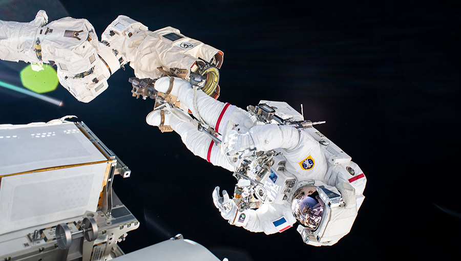 Astronaut Thomas Pesquet is pictured attached to the end of the Canadarm2 robotic arm during a spacewalk to install new roll out solar arrays.