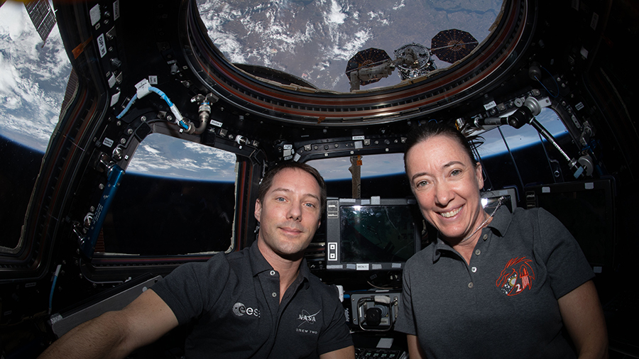 Astronauts Thomas Pesquet and Megan McArthur are inside the cupola with the Northrop Grumman Cygnus space freighter just outside behind them.