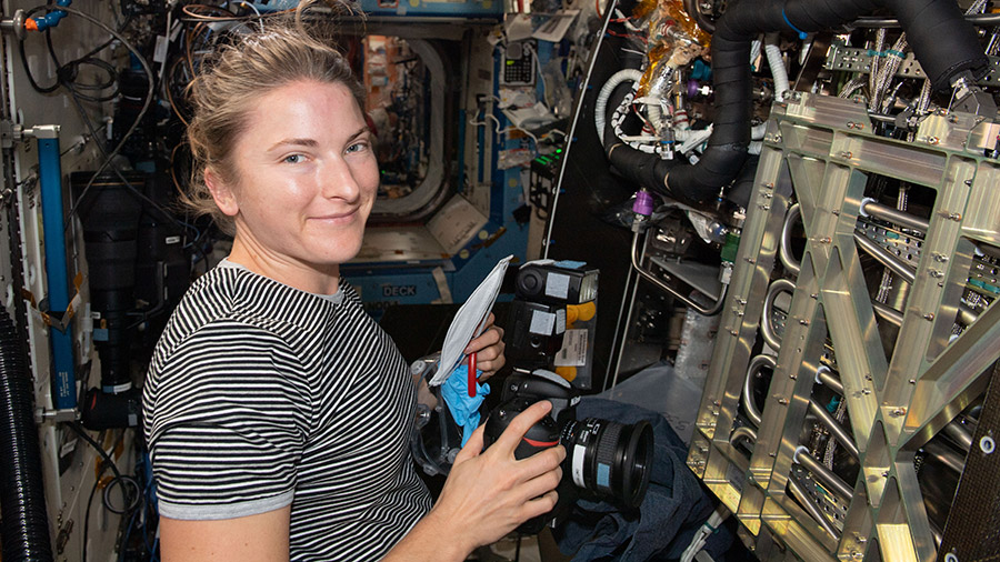 NASA astronaut Kayla Barron is pictured inspecting and photographing components inside the space station's Materials Science Research Rack.