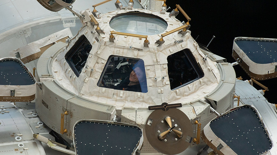 Astronaut Kayla Barron smiles while peering out from a window inside the cupola, the International Space Station's 