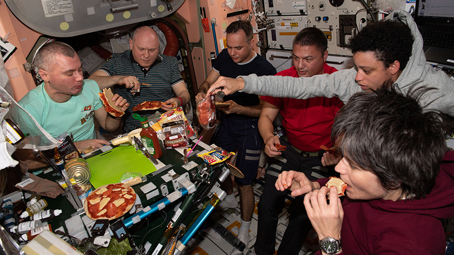 Expedition 67 crew members are pictured enjoying pizza during dinner time aboard the space station in May of 2022.