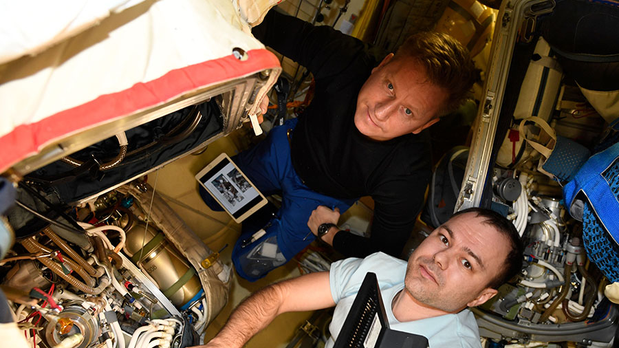 Cosmonauts (from top) Sergey Prokopyev and Dmitri Petelin work on an Orlan spacesuit inside the space station's Poisk module. 