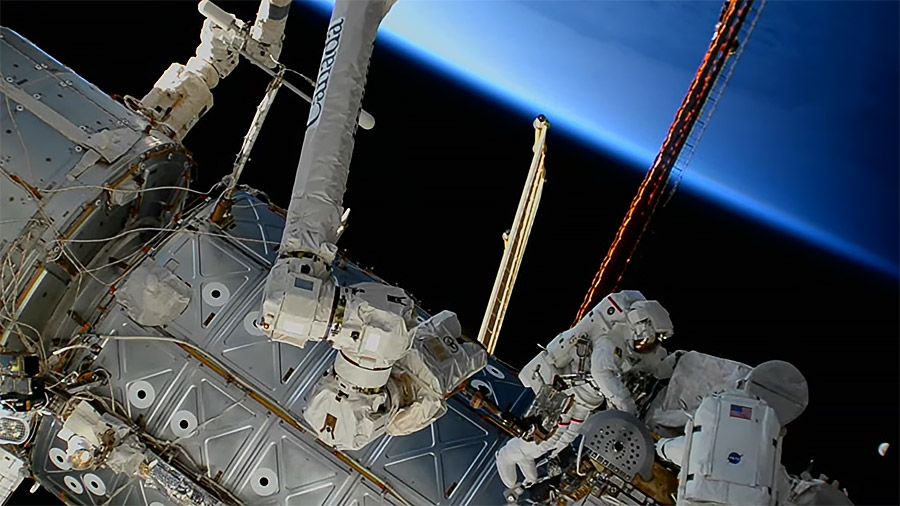 The Earth begins illuminating during an orbital sunrise as spacewalkers (lower right) Sultan Alneyadi and Stephen Bowen  work outside the space station. Credit: NASA TV