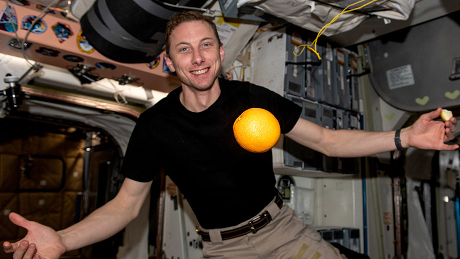 NASA astronaut Woody Hoburg shows off a fresh orange, recently delivered aboard the SpaceX Dragon resupply ship, flying in microgravity aboard the station.