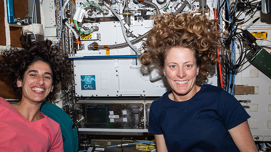 Astronauts (from left) Jasmin Moghbeli and Loral O'Hara pose for a portrait in front of the Cold Atom Lab. The physics research device observes the quantum behavior of atoms chilled to near absolute zero.