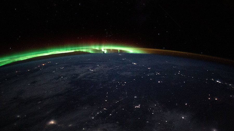 An aurora dances in the horizon of Earth's atmosphere as city lights shine through clouds cast over Mongolia while the International Space Station orbited 263 miles above.