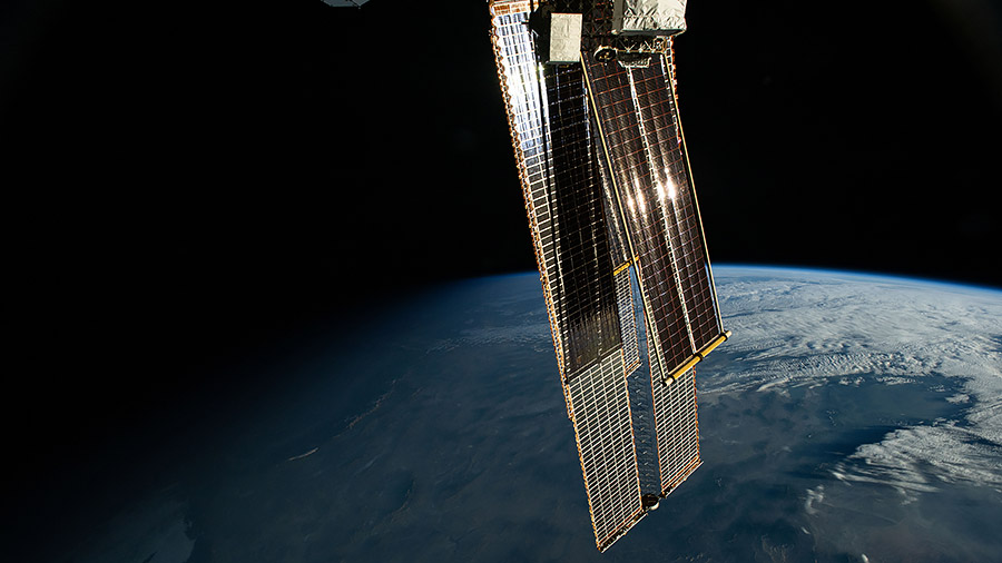 The first rays of an orbital sunrise reflect off the International Space Station's roll-out solar arrays that overshadow and augment the orbital outpost's main solar arrays.