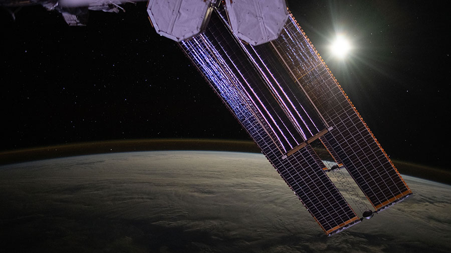 The Moon illuminates a cloud-covered Pacific Ocean as stars glitter in the background above the Earth's airglow. 