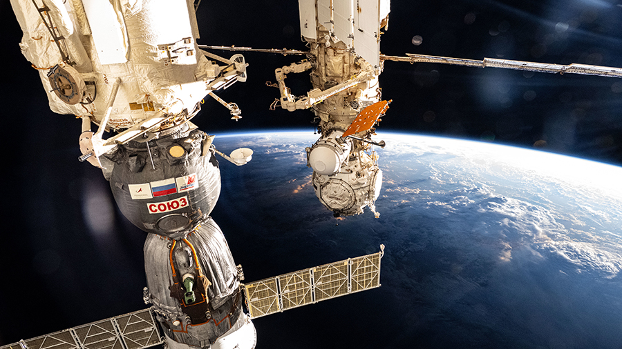 The International Space Station soars into an orbital sunset above the Pacific Ocean with the Soyuz MS-26 crew ship in the foreground and the Prichal docking module in the rear.