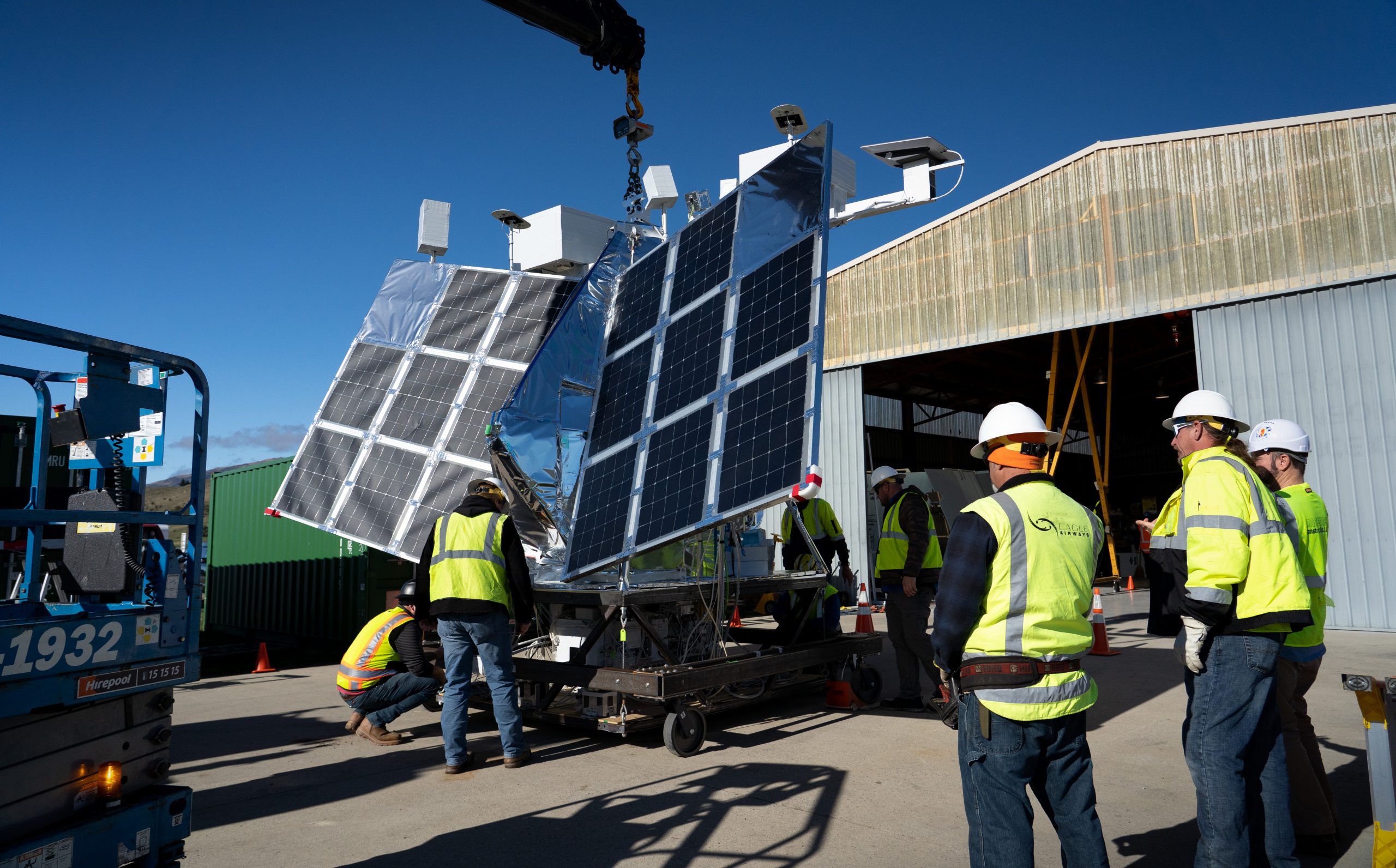 Technicians perform testing on a payload characterized mostly by its large solar arrays.