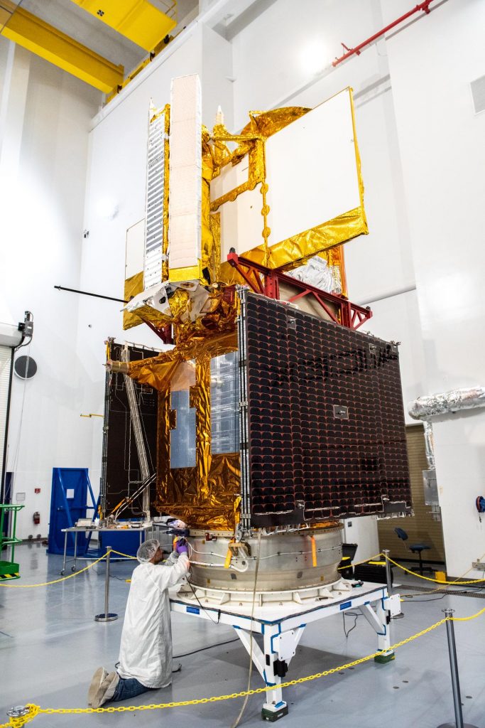 Inside the SpaceX facility at Vandenberg Space Force Base in California, a technician assists as a crane lowers the Surface Water and Ocean Topography (SWOT) satellite onto the payload adapter on Dec. 5, 2022. SWOT is scheduled to lift off aboard the SpaceX Falcon 9 rocket from Vandenberg on Dec. 15, 2022, at 3:46 a.m. PST. 