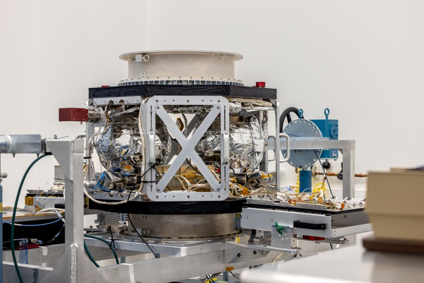 A spacecraft sits on a table in a clean room